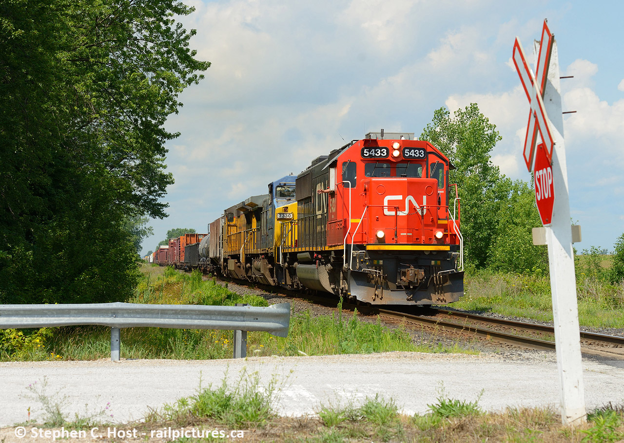 With a friendly wave from the hogger as an eastbound passes a rural crossing in the countryside east of Sarnia with a gaggle of 'if any of this led, that would be great' for motive power.

I usually plan my Sarnia visits quite meticulously, and after having told friends the day before I had no plans to go to Sarnia until the fall... My wife basically presented me a choice - go to the beach in Port Elgin (2 hours each way with nothing in between. UGH). So my rebuttal was if we're going to drive that far, let's just go to Sarnia and bring the kids to visit your parents instead. Check and mate. However, I had to explain to friends that "I'm not going to Sarnia, Hey, I'm in Sarnia" which they just make fun of me for now :)  Thanks to Tim Stevens I was able to intercept this en-route, back when the GECX and other leaders were prevalent, and just about anything would be found leading CN trains..So I have zero regrets for this trip, for it was productive. Other than the family functions,  I'd also capture a GECX (YN2) in the lead twice, a pair of GTW's on the Terra, and pair of GMD1's passing each other by the roundhouse. More to come.