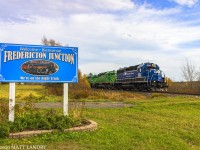 NBSR train 907 is westbound, heading out of Fredericton Jct, New Brunswick, passing the village sign. 