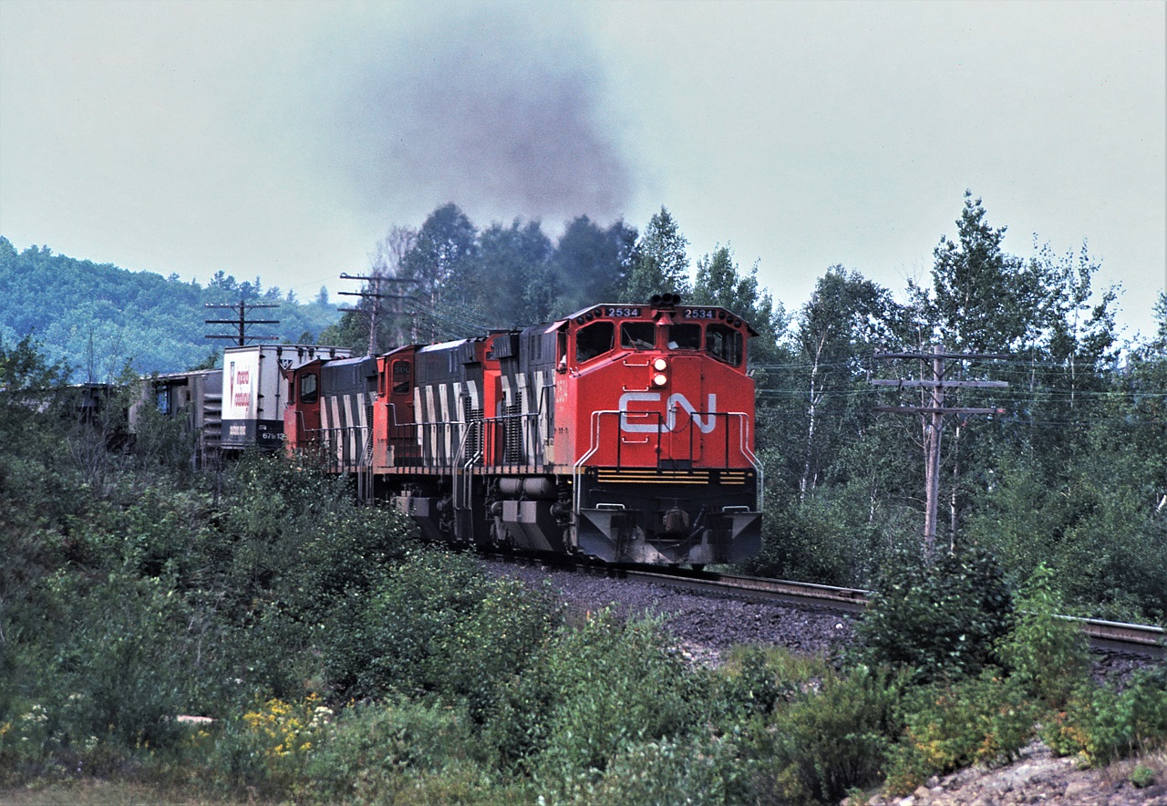 CN train 214 heads east out of Capreol, Ontario on the now abandoned Alderdale Subdivision with an all MLW power consist: 2534-2519-2500 and 74 loads 3 empties 5585 tons.  The train is shown approaching the Ella Lake road crossing.