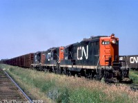 Three CN GP9's, 4411, 4499 & 4414, pull a string of pulpwood racks off the Kashabowie Sub into Neebing Yard in the west end of the Thunder Bay (former Fort William) area, passing a cut of 40' boxcars ubiquitous in these parts for hauling grain to the lakehead elevators. That mound of dirt piled on one of the pilot footboards is curious, maybe the unit hit a small washout somewhere along the line.<br><br>The lead and trailings units 4411 & 4414 were part of CN's first GP9 order (4400-4426, built 1955, originally delivered in the 1700-series) and featured the old-style Pyle "garbage can" headlights at both ends. Many later had a dual sealed-beam conversion plate added inside the housing, and eventually the entire headlight assemblies were changed out for more modern Pyle dual sealed-beam headlights. Other notable features are the long-hood bell (all of CN's early Geeps were long hood forward), the typical rooftop spark arrestors, early style "bolted" handrail stanchions, and the rectangular brackets welded to the front handrail stanchions (used for mounting CN's early-style removable ditch lights used out west). All three of these GP9's were later cut down and rebuilt as slugs 258, 219 & 234 respectively.<br><br><i>Original photographer unknown (duplicate), Dan Dell'Unto collection slide.</i> 
