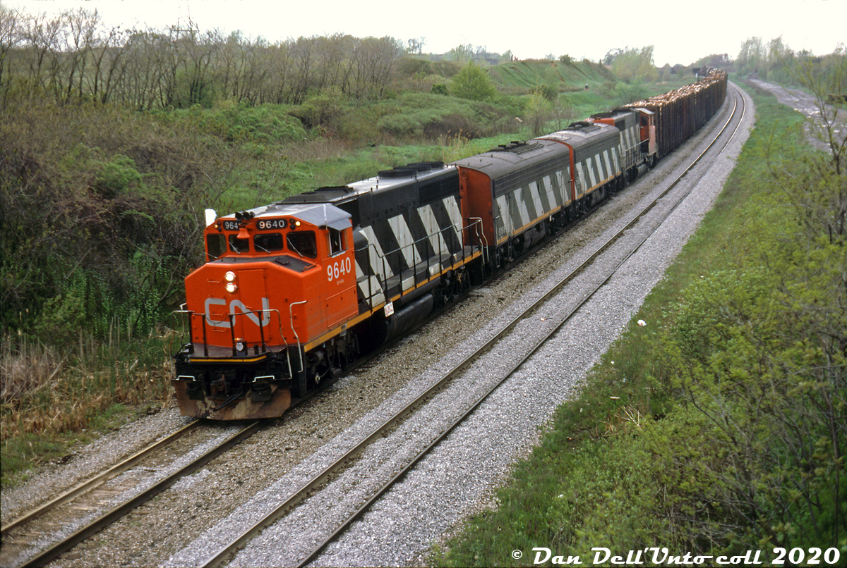 CN only rebuilt 10 of its GMD F7B freight B-units as part of their F7Au/F7Bu rebuild program in the mid-70's, but they got their mileage out of the cabless units and seemed to use them wherever they could, whether it was in pure A-B-A Sets of F-units or mixed in with other models at random.

Here on a less-than-ideal day, Reg was out to capture a rather unconventional lashup: CN GP40-2W's 9640 and 9656 splice F7Bu's 9198 and 9196, flying white extra flags on train #431 (with pulpwood racks up front) as they roll into Niagara Falls at Portage Road. The purists would scoff, but I suppose this qualifies as an "A-B-B-A" consist. The figures on the hill in the background are golfers enjoying some time on the course nearby.

Reg Button photo, Dan Dell'Unto collection slide (with some editing and cleanup)