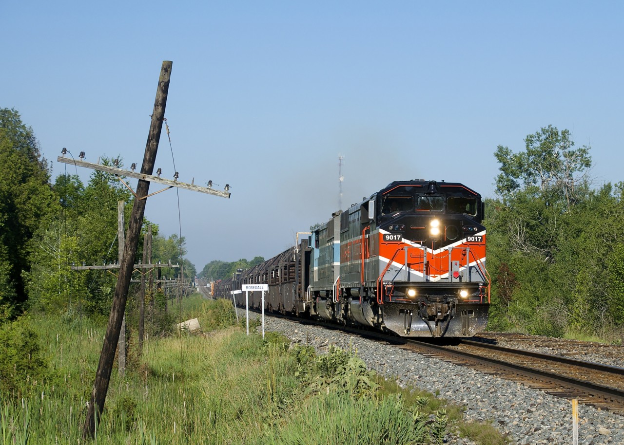 A rail train is passing the Rosedale station sign at MP 119 of CP's Winchester Sub, which is being converted from double track ABS to single track CTC. Power is CMQ 9017 and CMQ 9011 and the train is en route to pick up rail from the now ripped-up north track.