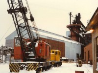 Unnumbered GE 50 Ton Center Cab and American Rail Crane Model 850-80 DE (Serial J3414) sit just north of the Company Engine house waiting their next assignment. In the background the 1912 built Blast Furnace sits as cold as the snow on the ground.  During the Second World War the operation had two (2) Blast Furnaces on site to support the war efforts.  To the left of the Rail Crane is the Pig Casting Machine(exterior to the High Bay), and behind the GE Center Cab are rail bound slag pots tilted on edge. Originally started as the Canadian Furnace Company by American investors from western New York, the operation joined the Algoma Steel Corporation in 1950.  The iron produced at the facility went under the brand name  "Victoria" Pig Iron and was the primary feed stock for iron foundries all over North America.  The image is looking south. Thanks to Paul O'Shell for the specs. on the American Crane.
