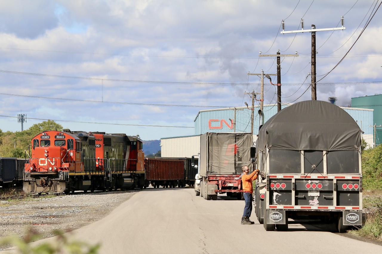 Hamilton has always built itself around the steel industry, in all of its forms, from raw steel coils, to new freight cars,as well as scrap metal and everything in-between. The full cycle can be found all around Hamilton. At Parkdale CN's International Bulk services building is used to offload everything from coils to large spools of wire while right next door a large scrap metal recycling facility loads gondolas. Here we see a truck driver unlatching his tie downs on his trailer as he waits for CN's local to clear the path to the CN transfer building. The crew of the train are busy collection gondolas full of scrap metal next door.