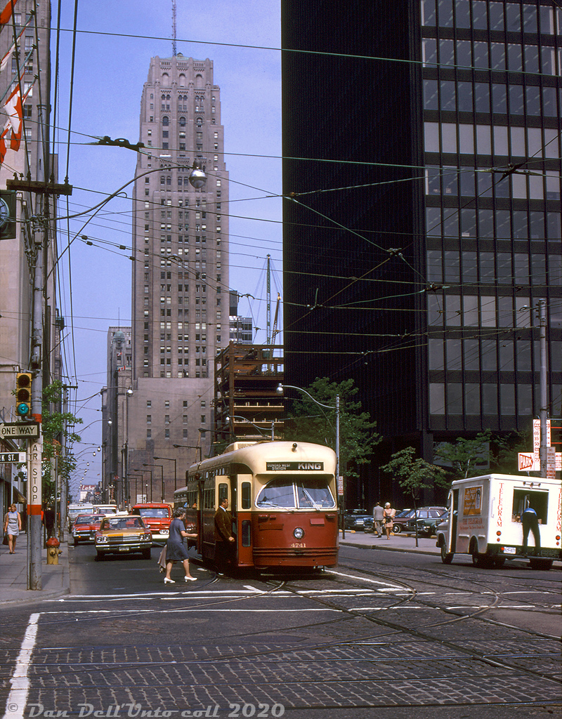 Toronto Transit Commission PCC 4741 (one of the A13-class streetcars originally built by Pullman for Birmingham AL in 1947) pauses amid skyscrapers at the corner of King Street and York Street in downtown Toronto to pick up waiting passengers. A Toronto Telegram van is seen pulled over on the side delivering papers, a year before the paper folded (later resurrected as the Toronto Sun). On the right is the TD Tower, completed three years earlier in 1967. Directly behind the streetcar towering prominent is the art deco Bank of Commerce (CIBC) building, built 1929-1931 as the tallest building in Toronto at the time (and in the British Empire). CIBC's Commerce Court West tower is seen under construction between the two.

Robert D. McMann photo, Dan Dell'Unto collection slide.