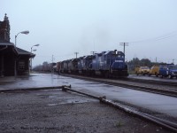  A quartet of Conrail GP38's (7998-7910-7999-7893) claws its way out of the Detroit River Tunnel with train ELDW-3 (Elkhart IN-Detroit/Windsor) and past Windsor Depot on a rainy June 14th 1981. The head end brakeman has bailed off and makes a dash for the shelter of the station where he will wait to make the cut for the Electric Yard. 
  Since the Electric Yard tracks were fairly short, only 45-50 cars, the yardmaster would give the cut number to the operator who would instruct the train, via radio, to stop when the cut was in front of the depot. The brakeman would then make the cut and the power would return after yarding the headend portion to yard the remaining cars. Sometimes a second cut may be necessary.
  ELDW's power would then return 'lite' back to Detroit. 