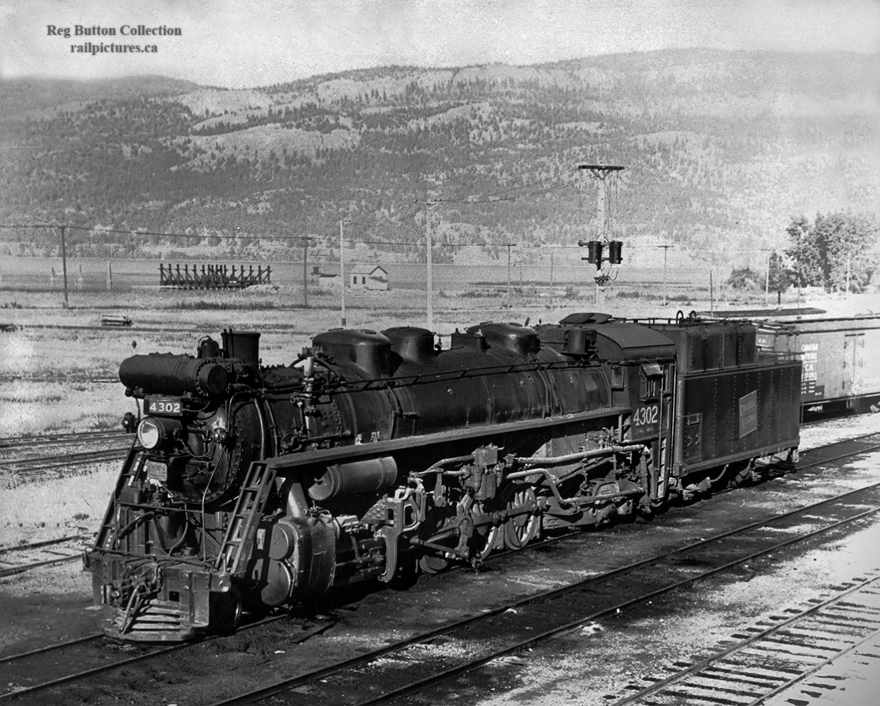 Tree covered mountains stand tall over Lake Okanagan and the town of Kelowna where we find CNR oil burner 4302 sitting in the yard.  4302 is T-4-a 2-10-2 built in 1929 by CLC as part of 15 locomotive order.  The CNR yard is long gone today, with the site now being occupied by condos, apartments, and Sunset Drive.Rails first reached Kelowna about 1909 on the Canadian Pacific Railway Okanagan line, running south from the transcontinental mainline at Sicamous to Vernon, then heading west to the lake at Okanagan Landing.  Cars were then barged to Kelowna, and offloaded by teams of horses into the small yard at the south end of town at the corner of Water Street and Smith Avenue.  Records show this operation continued into the 1950's using a truck and is detailed in this article from the Kelowna Daily Courier.The Canadian National Railway would complete it's line to Kelowna in September, 1925, completing a line which was begun in 1912 by the Canadian Northern Railway.  With this line built, CP would operate over it via trackage rights from Vernon in addition to the car ferry.  Passenger service was initially provided by an oil-electric car but was later replaced by standard equipment within a few months.  The CNR station, built in 1926, and opening January 4, 1927, served the passenger trains until 1967, when service was cancelled, and the station converted to a freight and express shed.  Designated a heritage structure in 1991, the station still stands today as The Train Station Pub.As traffic dwindled both CN and CP wanted to dispose of their Okanagan lines.  The Omnitrax shortline, Okanagan Valley Railway, took over the CPR operations in 1998 and operated through 2009 when their largest customer, the Owen-Illinois glass plant, shut down.  The Kelowna Pacific Railway would take over the CN operations in February, 2000.  The railway would go into receivership on Friday, July 5, 2013, with the rails being removed during 2015.  Passenger service briefly returned to Kelowna in 1999 as the Okanagan Valley Wine Train, operated by FunTrain Canada Inc., part of Nagel Tours of Edmonton.  The train, operating from Kelowna to Vernon, ran until 2003 when the operation was suspended due to lack of funding.Thanks to Steve Host and Dan Dell'Unto for editing assistance.