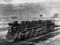 Tree covered mountains stand tall over Lake Okanagan and the town of Kelowna where we find CNR oil burner 4302 sitting in the yard.  4302 is T-4-a 2-10-2 built in 1929 by CLC as part of 15 locomotive order.  The CNR yard is long gone today, with the site now being occupied by condos, apartments, and Sunset Drive.<br><br>Rails first reached Kelowna about 1909 on the Canadian Pacific Railway Okanagan line, running south from the transcontinental mainline at Sicamous to Vernon, then heading west to the lake at Okanagan Landing.  Cars were then barged to Kelowna, and offloaded by teams of horses into the small yard at the south end of town at the corner of Water Street and Smith Avenue.  Records show this operation continued into the 1950's <a href=http://www.okanagan.net/ocarc/chapman.jpg>using a truck</a> and is detailed in <a href=http://www.okanagan.net/ocarc/chapman2.jpg>this article</a> from the Kelowna Daily Courier.<br><br>The Canadian National Railway would complete it's line to Kelowna in September, 1925, completing a line which was begun in 1912 by the Canadian Northern Railway.  With this line built, CP would operate over it via trackage rights from Vernon in addition to the car ferry.  Passenger service was initially provided by <a href=http://www.okanagan.net/ocarc/feb18,1926CN-oil-car.jpg>an oil-electric car</a> but was later replaced by standard equipment within a few months.  <a href=http://www.okanagan.net/ocarc/station.jpg>The CNR station,</a> built in 1926, and opening January 4, 1927, served the passenger trains <a href=http://www.okanagan.net/ocarc/ts_archive1968.jpg>until 1967,</a> when service was cancelled, and the station converted to a freight and express shed.  Designated a heritage structure in 1991, the station still stands today as <a href=https://www.teamconstruction.ca/wp-content/uploads/2019/05/Capture-1.jpg>The Train Station Pub.</a><br><br>As traffic dwindled both CN and CP wanted to dispose of their Okanagan lines.  The Omnitrax shortline, <a href=http://www.railpictures.ca/?attachment_id=9687>Okanagan Valley Railway,</a> took over the CPR operations in 1998 and operated through 2009 when their largest customer, the Owen-Illinois glass plant, shut down.  The <a href=http://www.railpictures.ca/?attachment_id=1158>Kelowna Pacific Railway</a> would take over the CN operations in February, 2000.  The railway would go into receivership on <a href=http://www.okanagan.net/ocarc/okanagan-rail-connection-severed-7813.pdf>Friday, July 5, 2013,</a> with the rails being removed during 2015.  Passenger service briefly returned to Kelowna in 1999 as the <a href=http://www.railpictures.ca/?attachment_id=10769>Okanagan Valley Wine Train,</a> operated by FunTrain Canada Inc., part of Nagel Tours of Edmonton.  The train, operating from Kelowna to Vernon, ran until 2003 when the operation was <a href=http://www.okanagan.net/ocarc/wtcancl.gif>suspended due to lack of funding.</a><br><br>Thanks to Steve Host and Dan Dell'Unto for editing assistance.