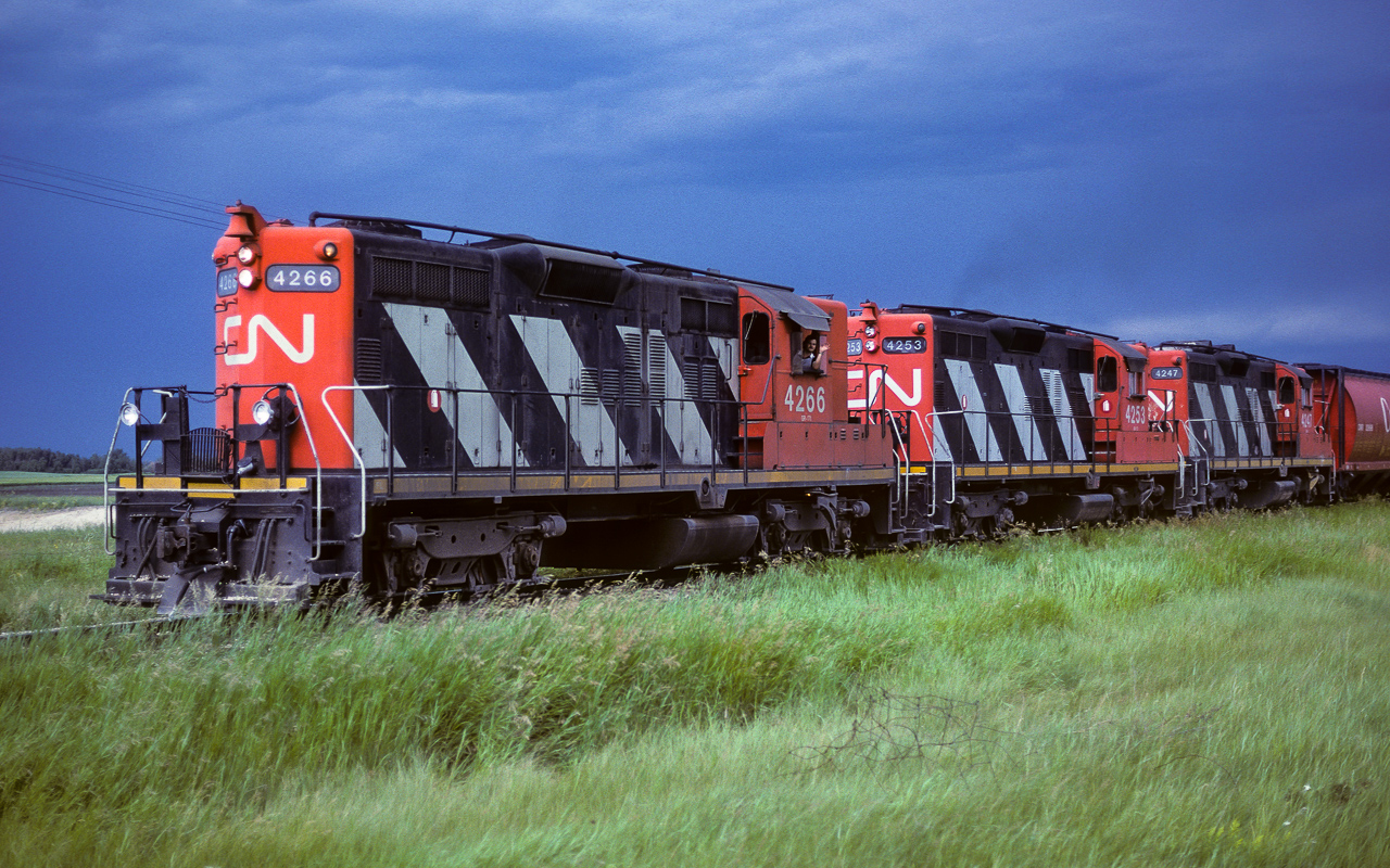 Trains to Fort McMurray this week were running way off their usual times. I believe the track was undergoing considerable upgrading, which brings about operational delays of some nature. The Muskeg Mixed usual return was in the early morning hours, during the night. Here it is coming home at 16:15, very late indeed. There were storms in the area, producing this interesting light. Just immediately west of here, the sky is blue with the sun out. Although I have clouds above me, the scene is being lit by the bright sky to the west. The late return has not put a frown on the brakeman. Photo taken a couple of miles west of Redwater. Please see neighbouring post for part-2.