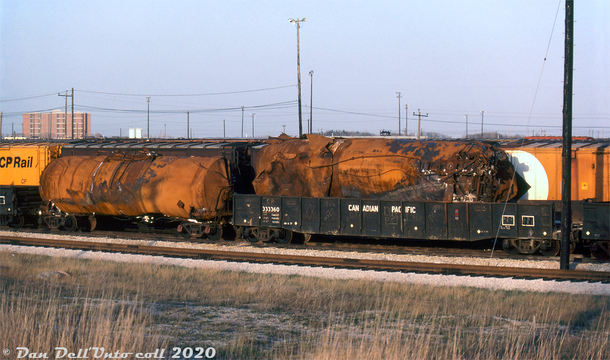 Some of the tank cars involved in the November 10th 1979 Mississauga train derailment sit in CP's Toronto (Agincourt) Yard, presumably kept for inspection during the aftermath investigation. As most know, a tank car on an eastbound CP freight had a hox box that caused a large derailment on the Galt Sub at Mavis Road grade crossing in Mississauga, including some chemical tank cars that derailed and caught fire and/or exploded. A load of leaking chlorine gas in one of them caused mass evacuation of much of the city as fire crews tried to contain the blaze and stop the leak.

Two tank cars in particular are shown here. The wrecked one in CP gondola 333360 appears to be chalked UTLX 29327 or 77 on the bottom. A less-manged one is riding on its own, likely on some shop trucks or spares off the wreck auxiliary train that rerailed it.

Keith Hansen photo, Dan Dell'Unto collection slide.