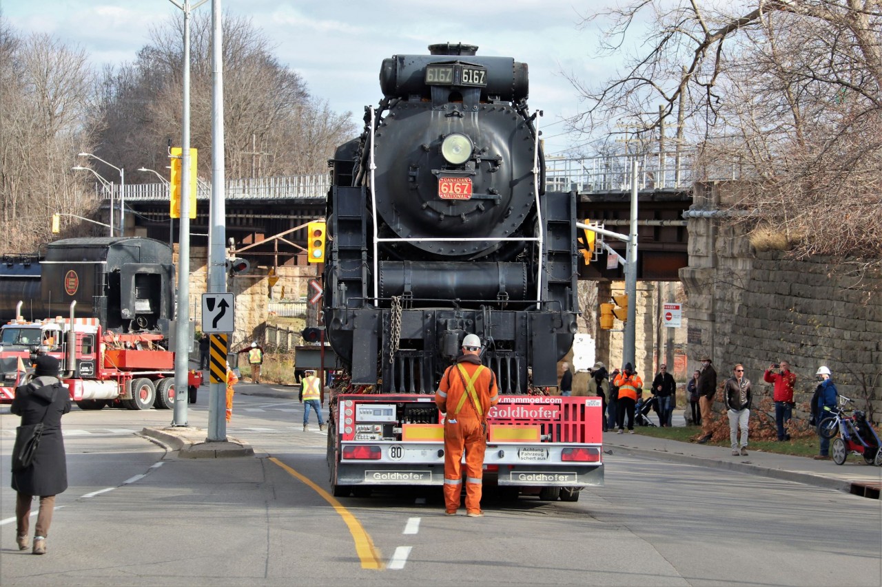 Well the big move of steam locomotive CN 6167 is upon us. With the expansion of the GO facilities at the station, it was either scrap, sell or relocate this consist that has been a fixture in Guelph for many years so the decision was made to move it to a new location along the Speed River. With the tender already being slowly backed in to its new location by the Mammout transport truck in the background, CN 6167 sits on the remotely controlled trailer at the stop lights at Macdonell Street awaiting its turn to be fitted in to its new home.