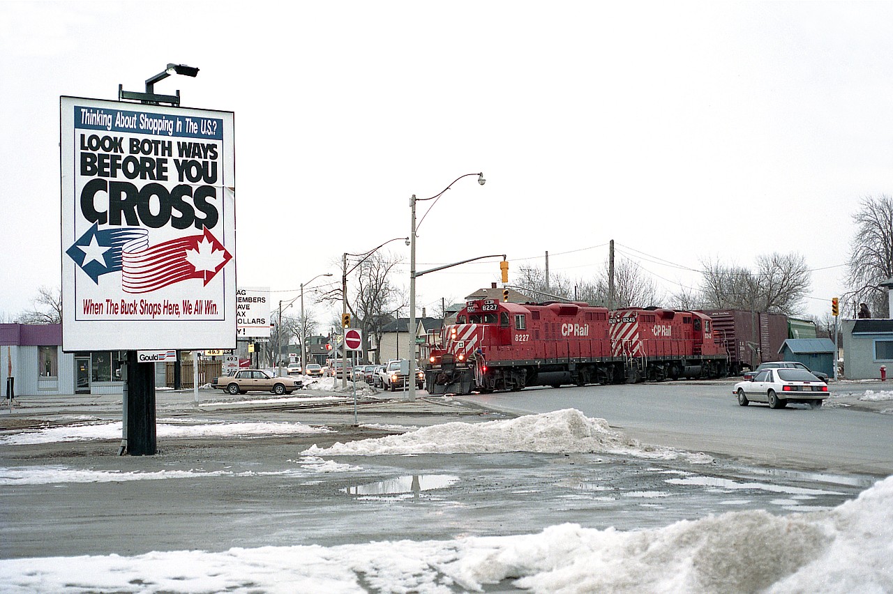 Back in the day, not all that long ago.  The Canadian and American dollar were almost at par; the locals were streaming to the USA to take advantage of the fact and get their "cheap" groceries & gas.  A billboard campaign to try and slow the tide (seen on the left) really had little effect. Back in the day GP9 locos seemed to be everywhere on the system, and better, there were lots of trains and rail traffic in Niagara Falls. Not any more. The CN yard is desolate, the CP Montrose yard is gone; the CP main thru the city is gone as well as this connector and to see anything in trains at all, one has to wander down to Fort Erie in hopes something is rolling by the defunct CN yard down that way. How times change!!  The image here is CP 8227 and 8246 heading back to Montrose from the CN yard, crossing thru the intersection of Victoria and Bridge Sts.    Nostalgic.