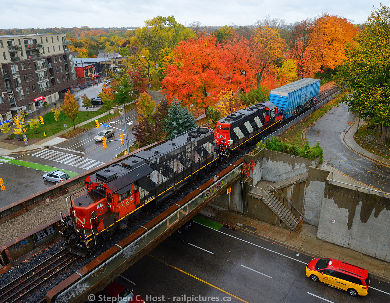 CN L540 departs Guelph for Acton with a huge train in tow. A Red Top Taxi is heading south on Norfolk St, once upon a time this was an at-grade crossing (hard to believe). Fall is in full effect and red-topped trees are at peak colour. THis is about where I photographed this in 2016. While I was taking this shot a wild Jacob Patterson appeared!