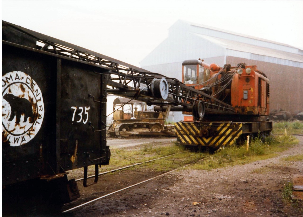 American Rail crane Model 850-80DE Serial J-3414 delivered to Canadian Furnace (Algoma Steel) in 1957 sits idle with Algoma Central Gondola 735.  The rail crane had completed the yard clean up of Victoria Pig Iron and would soon be sent north to ALGOMA STEEL in Sault Ste. Marie.  Gondola 735 is not likely to be found on any rolling stock lists for Algoma Central and was part of the home fleet of in-house cars, some of them labelled as Algoma Central and some as Canadian Furnace. The Casting house is the building in behind and the old school bulldozer lacks the creature comforts of today's "yellow goods".  It would have been used to scrape the pigs that were stuck in ground so the rail bound mag. crane could load them into the gondolas.  Thanks to Paul O'Shell for the rail crane information.