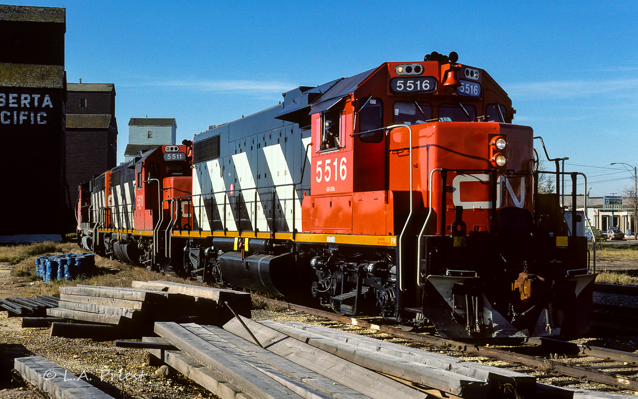 The bi-weekly grain extra was making a stop at the Redwater elevators on a sunny Fall day. The 5516, 5511 and 5592 almost have the cars at their mark as the engineer, with handset out the window, replies an affirmative "half a car". The 5516 looks to have been through the wash rack very recently. The lumber pile in the foreground did disappear over the next year or so. Many of the grade crossings were redone, making a number of them much smoother to negotiate.