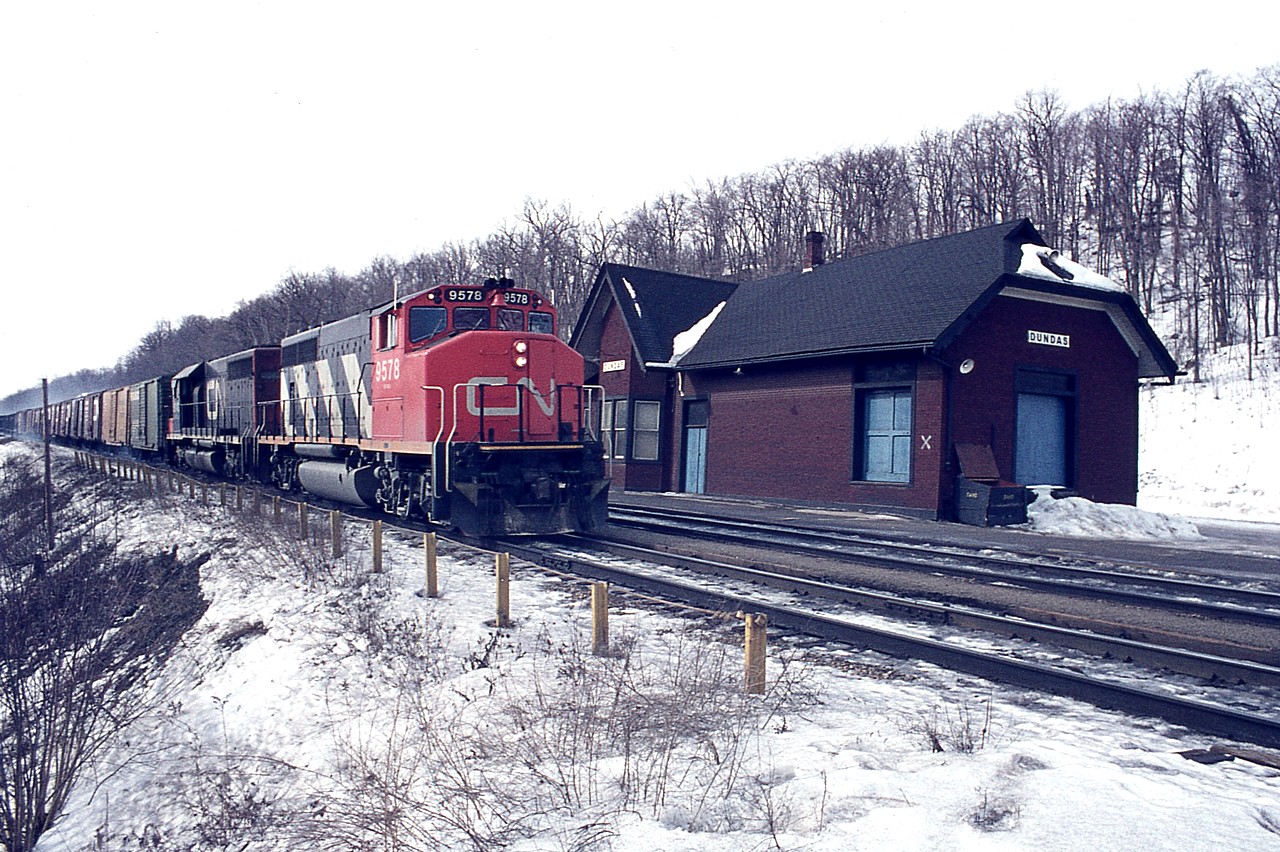 A typical dreary day in February and I find myself on a day off work hanging around the old Dundas station. It was a change from Bayview and presented some interesting scenery. And I always loved shooting trains with a station included, as it was stations that got me into this hobby in the first place.
So, eastbound is CN 9578 and 5046 with a long string of boxcars and mixed freight behind. A couple of passenger trains still stopped at Dundas station back then, so I was pretty well guaranteed the parking lot would be clean. 
 This image shot using Woolco slide film, and held up remarkably well.