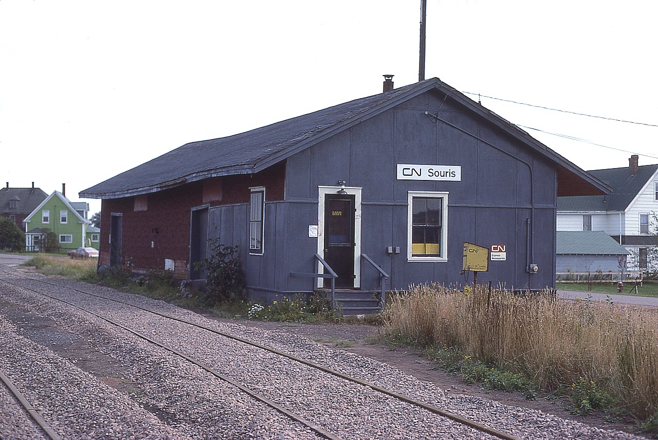 This rather sad looking building as photographed back in 1981 I am posting here just for those interested in Prince Edward Island and it's railroad history. It is not much to look at, but in 1981 it was an old freight shed converted to station. The way freights stopped here on their infrequent visits, crews and maintenance personnel used the building in which to do their paperwork. Curiously, there is a "VIA" decal on the door, yet passenger service ceased here in 1968. I'm guessing perhaps someone could stop in and order tickets for the bus out of Charlottetown?
Originally Souris had a passenger depot built between Souris East and Souris West, around 1876 as the town was divided by the wide and slow mouth of the Souris River. The station was built on a moving sandbar! Worse, tides affected the rails, and often sand covered them and had to be swept away. Such was the early days of the PEIR. A second station was built in 1879 on stable land in Souris East.
That station lasted until 1971 when vandals burned it to the ground. So the freight shed pictured was now "the station" in town.
Souris has been going thru troubling times. The population, just over a thousand, is declining. It was settled first in 1727; and early settlers had endless troubles with huge mouse populations. Actually, "Souris" is the French word for "mouse", and that little furry you-know-what is the town mascot.
The station, or whatever you want to call it, is now long gone.