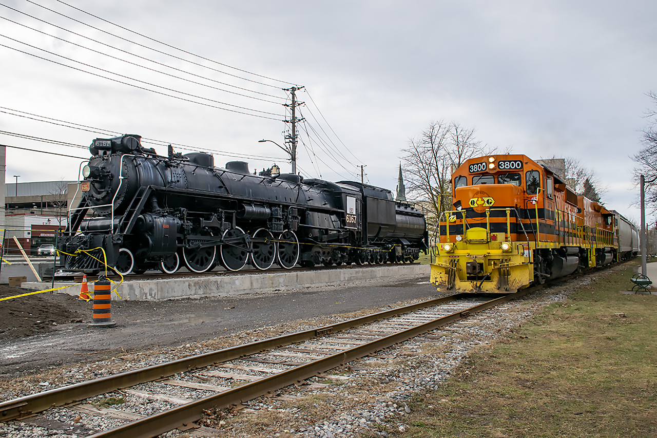 The Guelph Junction Railway, operated by the Goderich & Exeter railway passes by locomotive 6167 in her new spot at John Galt park. On November 14th 6167 was moved from her home by the Guelph Central Station to this location by the GJR. The move was necessary due to Metrolinx's plans to expand the station. Obviously the area is still under construction, as evidenced by the safety ribbons and pylons. Eventually there will be a nice pathway around the locomotive. 

 Interesting note, 6167 sits directly at the site of the Priory, the first building in Guelph. Built by Guelph founder John Galt. The Priory would also serve as the first post office, and when the CPR arrived in Guelph in the 1880s, it became the CPR station. The Priory was replaced by a stone station built around 1910. This area is a highly significant area to Guelph, and its railway history. A fitting spot for 6167.