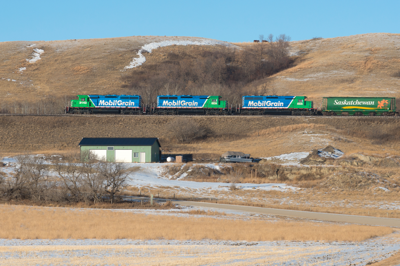 Mobile Grain's Last Mountain Railway makes it's way up the notable grade and out of the valley at Lumsden with three clean SD40s for power. On a  side note, if I had a shop like the one in the foreground, I don't link I'd ever need to go in the house again!