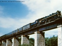 High above Trout Creek, CNR 4-8-4 6200 approaches the <a href=http://www.railpictures.ca/?attachment_id=32008>station at St. Mary's</a> with Saturday only passenger train 111 bound for London, having departed Toronto Union station at 12:10h.  If on the advertised the time should be 16:12h with final arrival at London at 16:45h according to <a href=https://s3.amazonaws.com/content.sitezoogle.com/u/131959/ad89b09c628e8183bb66367faa0a6e8effc73050/original/1957-cnr-ee-tt-12-sont-dist-stratford-london-div-19571027-chris-mawdsley.pdf?response-content-type=application%2Fpdf&X-Amz-Algorithm=AWS4-HMAC-SHA256&X-Amz-Credential=AKIAJUKM2ICUMTYS6ISA%2F20201223%2Fus-east-1%2Fs3%2Faws4_request&X-Amz-Date=20201223T030215Z&X-Amz-Expires=604800&X-Amz-SignedHeaders=host&X-Amz-Signature=4de011c8dcb4cd40e9b3f9a08f084522234bfed89530c27058127112fa8cdf7b>1957 employee timetables.</a><br><br>Built by Montreal Locomotive Works and <a href=http://www.trainweb.org/oldtimetrains/photos/cnr_steam2/6200a.jpg>delivered in June 1942,</a> 6200 is a <a href=http://www.cnrha.ca/sites/default/files/styles/node_gallery_display/public/node_gallery/u-2-g.jpg?itok=nB8li4eP>U-2-g 4-8-4</a> and the first in an order for 35 of such locomotives.  After retirement at the end of the steam era, 6200 would be donated to the National Museum of Science & Technology in Ottawa where it sits on display on the museum's front lawn.  The locomotive has recently <a href=http://www.railpictures.ca/?attachment_id=35267>undergone cosmetic restoration.</a>  Two other U-2-g locomotives are on display; <a href=http://www.railpictures.ca/?attachment_id=24104>CNR 6213 in Toronto,</a> and <a href=http://www.railpictures.ca/?attachment_id=10469>CNR 6218 in Fort Erie.</a>