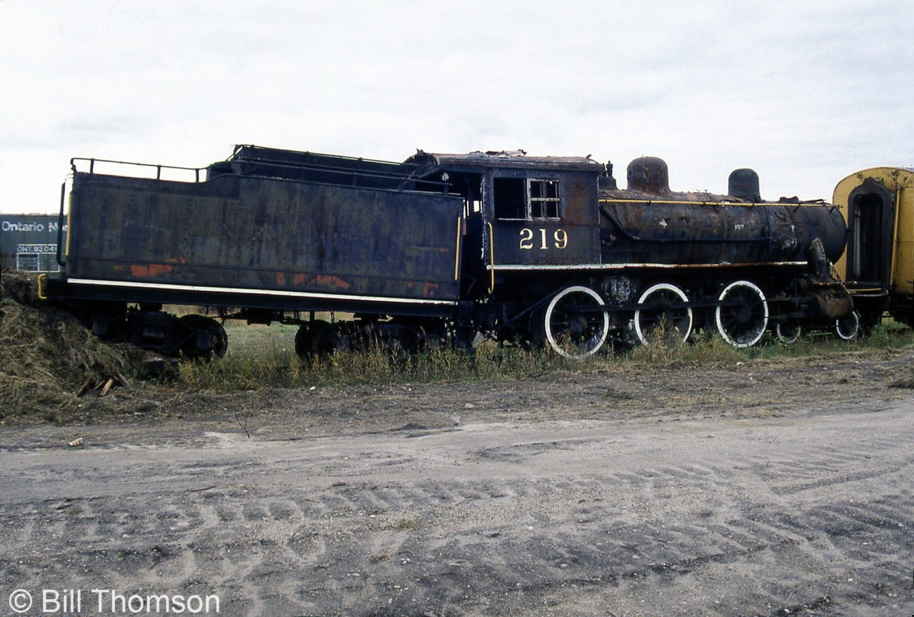 Normetal Mining 219, a former Temiskaming & Northern Ontario Railway 4-6-0 steam locomotive, is seen stored in the Ontario Northland Railway's yard in Cochrane ON in October 2000. At the time of this photo it had been stored in Cochrane for nearly two and a half decades and was is looking more than a little worse for wear, haphazardly stored out of the way at the end of a yard track with the rear tender truck shoved up against a pile of ties and dirt mount.T&NO 219 was built by MLW in 1907 as one of six 4-6-0 units, originally numbered 119 and later renumbered 219. TN&O sold the steamer to Normetal Mining in Quebec in 1938 who used it for industrial switching. It was sold to a private owner in 1976 who had dreams of running excursions with it on the Spruce Falls Power & Paper Company line. It was moved to Ontario Northland in Cochrane for work, but the owner passed away and plans fell through, so eventually ONR came into ownership of the old engine. 219 was stored for nearly three and a half decades in by ONR in Cochrane until 2012, when it was sold off and acquired by the Northern Ontario Railroad Museum & Heritage Centre (NORMHC), who moved it to their museum in Capreol in 2014.