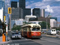 A fairly modern 1980's view of the downtown Toronto skyline shows a nice variety of architectural styles in this selection of skyscrapers (before the present-day glass-clad everything style took over). TTC 4301, an A13-class PCC streetcar built new for Toronto in 1947, operates on the 504 King Street route, stopped westbound at John Street (note the blue illuminated street sign box, always a nice touch). In their final years in service, much of the TTC PCC fleet suffered through the indignity of large font numerals slapped over the original (smaller) painted out numbers. The water bumpers, while a neat concept, were also somewhat unsightly.<br><br>By this point in time, the old <a href=http://www.railpictures.ca/?attachment_id=30801><b>CP/Dominion Express freight sheds</b></a> that used to be in the King/Simcoe area had been knocked down a number of years prior and replaced with the new Roy Thomson Hall, while the rest of the property remained parking lots until eventual redevelopment into Metro Hall (that parking lot gained notority in the opening scene of the film "Police Academy", filmed in Toronto). "Honest Ed" Mirvish, best known for his Bathurst & Bloor discount store, also owned a line of storefronts on this stretch of King Street including the Royal Alexandra Theatre, Ed's Warehouse (restaurant - roast beef and steak), Ed's Chinese, and Old Eds (although most closed over time). The tower crane in the background hints at greater things than parking lots to come in the next few decades for Toronto's downtown core.<br><br><i>Glenn Smith photo, Dan Dell'Unto collection slide.</i>