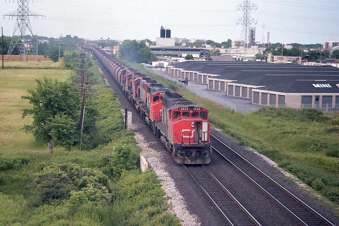 Once a familiar sight, the Dofasco Ore train has been gone since around 1990 when profitability ceased. The train I would think ran most often with 5 gp40-2L wide bodies; as seen here. We note CN 9529 as leader, I have no idea where my notes went on this one, so no numbers for the rest of the power other than the second unit visible. I shot this from the QEW bridge over the tracks, so maybe my paper blew away. :o) In the extreme background you can see on the right the old Freeman Station opposite where the 90 or so ore cars are coming off
the Halton sub. The train was handed to the CN from the ONR.
"A/C" door open..it must have been a warm day. I forget.