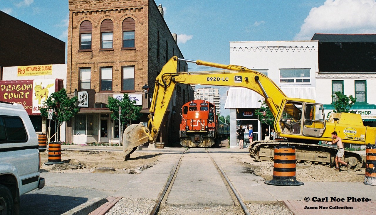 Also during 1997, King Street in Uptown Waterloo was undergoing a large-scale construction project and the CN 15:30 Job is viewed now stopped between the buildings at King Street after observing a piece of equipment blocking the right-of-way. 
The CN crew eventually got the attention of a few lingering construction workers that were luckily still there and after realizing their error, one worker quickly moved to rectify the situation. Once given the all clear, CN 4134 and 4137 would continue through Waterloo with nine-ex VIA Rail coaches for WSJR as well as their regular cars for customers in Elmira on the Waterloo Spur.