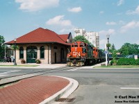 During summer 1997 the railway scene in Waterloo, Ontario was buzzin with activity. The long awaited Waterloo-St. Jacobs Railway (WSJR) had finally arrived and the newly constructed station near Erb and Caroline Streets had been completed and was ready to go. The former Les Trains Touristiques du St-Laurent had arrived that June complete with two FP9u’s along with several passenger cars. Following the bankruptcy of Les Trains Touristiques du St-Laurent, WSJR had purchased all the equipment at an auction. The future was bright and the Waterloo Spur to Elmira was being given an injection of new life with FP9’s now powering long-awaited tourist trains between Waterloo and St. Jacobs much like a retro throw-back to the CN passenger excursions that had powered Sugar Bush Express excursions to Elmira during the 1970’s. 
<br>
While the WSJR was now busy operating on the spur, CN continued to provide regular freight service to industries on the line at Waterloo, St. Jacobs and Elmira that were all still frequently receiving cars. While both WSJR and CN operated separately, there were rare occasions when the two interchanged equipment. One instance was the highly anticipated move of former VIA Rail coaches that WSJR had also purchased to operate with their newly acquired equipment from Quebec. 
<br>
Here in the sweltering heat of a summer afternoon, CN GP9RM’s 4134 and 4137 are seen about to cross Regina Street in Uptown Waterloo as they slowly haul nine-ex VIA Rail coaches for WSJR as well as their regular freight traffic for Elmira, which required the use of two units on this day’s CN 15:30 Job. 
