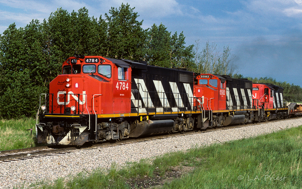 Here is a 31 and a half year contrast with Jason Noe's recent post of the 4784. In this photo, it has only in the last few weeks been renumbered. It's stablemate following is still waiting for the 47's. The units are looking very good for 15 years old. Also, as in Jason's picture, there is a GP9 helping out in the rear. A flatcar with wooden ramps heads up an otherwise solid train of empty hoppers.
