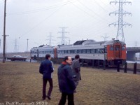 It looks like someone didn't have their railfan filter on their lens (anyone look familiar here?). The Upper Canada Railway Society held a fantrip on March 9th 1974 using CN "Railiner" RDC cars 6106 and 6111 that toured the Toronto Bypass (York & Halton Subs) and Beach Sub on a trip between Pickering and Stoney Creek, which included a special run down the Milton Townline Spur across the CN-CP diamond to Milton Station, and a trip down the Beach Sub (with a photo stop on the lift bridge at Hargrove). Here, a photo stop ensues near Stoney Creek as the two RDC's proceed south with a crewmember flagging the Van Wagners Beach Road crossing near Beach Blvd. The QEW is visible on the right, where Beach Blvd. ducks under it.<br><br>The gloomy weather foreshadowed the fate awaiting the CN Beach Sub (aka the "Beach Branch") in the near future. Most CN mainline traffic used the more popular Oakville & Grimsby Sub mainlines through Hamilton, and the old Beach Sub (originally part of the Hamilton & North-Western Railway) between Stoney Creek and Burlington was soon to be severed into two spurs by QEW freeway construction that took place in 1974-1975 (which included removal of the famed QEW traffic circle). The main spur ran south from Burlington to service a customer near Stoney Creek for a few more years, but was later abandoned in 1981 and removed, leaving only short stubs on either end.<br><br><i>Gord Taylor photo, Dan Dell'Unto collection slide.</i>