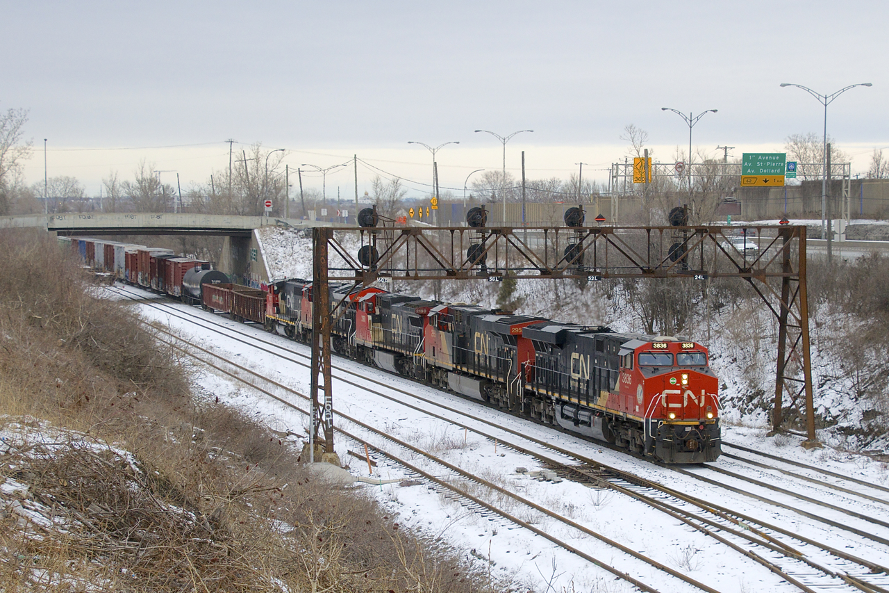 A long CN 527 has five units (CN 3836, CN 2952, CN 2190, CN 3086 & CN 9677) as it ducks under a signal bridge on the approach to Taschereau Yard. This angle just opened up recently when a large amount of bushes and trees were cut here.