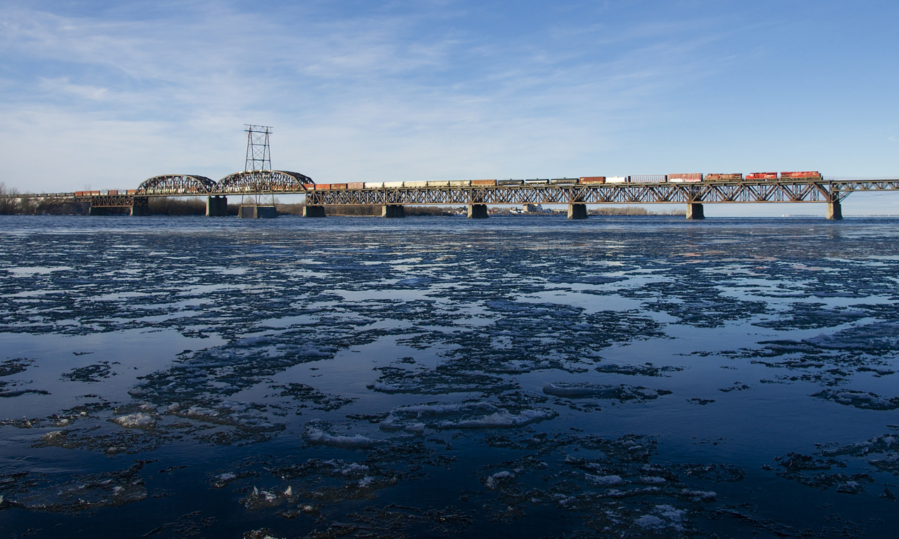 Normally into Montreal before sunrise since a schedule change at the end of last summer, CP 253 has been delayed by a broken rail further south, allowing it to enter Montreal in daylight. Here it crosses the icey St. Lawrence River with CP 8869, CP 2228, CP 9705 and 57 cars.