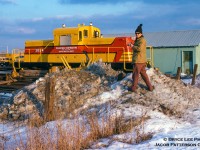 Now who might this be? This individual tagged along with Bryce Lee on a chilly February afternoon in 1977 to check out Penvidic Contracting's ex-CPR 44-ton CLC D-T-C 44H44A1 switcher in a sharp company paint scheme. Note the scheme design is based off the CP maroon and grey it once wore. Built by Canadian Locomotive Co. of Kingston and outshopped on April 29, 1960 as CPR 19, the locomotive was one of 14 D-T-C (Diesel Torque Converter) locomotives, also called DT2s, designed for light switching duties and to be operated without a fireman (weighing less than 45 tons). After it's 12-year career with the CPR, this unit was sold to Penvidic Contracting of Burlington in November, 1972, where it would be involved in a deadly accident while working on the construction of Hydro One's Trafalgar Substation line, branching south off the Galt Sub at the east end of Hornby yard. During the workmen's coffee break on March 14, 1978, the locomotive ran away down a small grade, smashing into cargo vans positioned close to the tracks near where the workers stood. 3 perished, including the engineer who had attempted to board and stop the movement. After an inquest into the incident, the locomotive would be sold in April, 1980 to Aquitaine Petroleum and sent to work at their gas plant in Ram River, Alberta <a href=http://www.railpictures.ca/?attachment_id=44036>(which also rostered Canada's only ALCO C415s)</a> as their 2034, later to it's original number of 19, and relettered for Aquitaine's new owner, Canterra Energy. It's final operation would be with Skibstead in Rosebud, Alberta before being retired in September, 1987 and put <a href=http://www.mountainrailway.com/Roster%20Archive/CP%2010/CP%2019-4.jpg>on display in Champion Park, Okotoks, Alberta.</a><br><br>Bryce's shot once <a href=http://www.mountainrailway.com/Roster%20Archive/CP%2010/Penvidic%20Contracting%202034-1.jpg>he climbed up the snowbank.</a><br><br>More DT2s:<br>

Dan Dell'Unto Collection: <a href=http://www.railpictures.ca/?attachment_id=34841>Dryden, Ontario.</a><br>
Bill Hooper: <a href=http://www.railpictures.ca/?attachment_id=41339>Canal Flats, British Columbia.</a><br>
Bill Thomson: <a href=http://www.railpictures.ca/?attachment_id=29867>Goderich, Ontario.</a><br>
Bill Thomson: <a href=http://www.railpictures.ca/?attachment_id=29653>Tottenham, Ontario.</a><br><br><i>Bryce Lee Photo; Jacob Patterson Collection slide.</i>