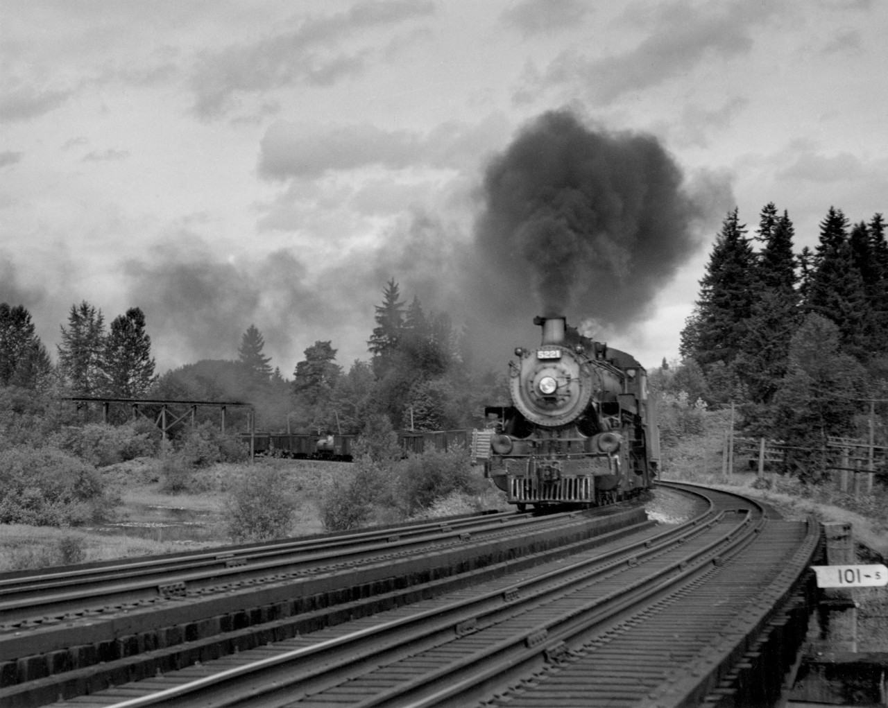 August 24, 1948 CP M-810 (mixed 810), which operated from Vancouver to Sumas, where it connected (freight) with the Northern Pacific.  Train was the remains of a once deluxe service which connected Vancouver with Seattle with sleeping cars, on a night run.  One of the Sleeping conductors on this run had been a Mr. Taylor, father of Cecil Taylor, General Clerk in Manager's office, who retired prior to 1967.  Train is seen here 29 miles east of Vancouver, BC, or 101.5 miles west of North Bend.  Consist: 20 cars; last is a combination, which can be seen in photograph.  Old bridge high in background used to be used in some logging railroad to bring logs from mountains on north down to the Fraser river.  Engine, 5221 was originally built in 1911, or approximately, and numbered in the 1800 series.  Then it was renumbered to the 3600 or 3700 series, Class N-2, and in these two series (1800 & 3600) was a 2-8-0.  Now, as a 5200 series, and P class, it is a 2-8-2 and resembles in specifications other P-1 class power.  The conversion of 3600 & 3700 (N-2 class) power to Mikes took place late in the road's steam era, between 1946 and 1949.
