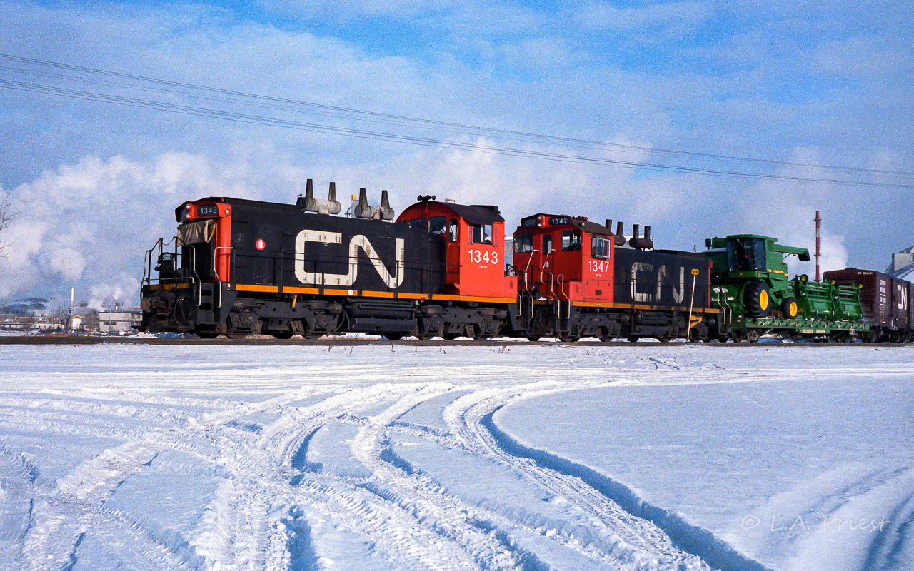The 1343 and 1347 are making a long reach into the Sherritt Gordon fertilizer plant, located directly east of the City. The 1347 is one of the very few 1300's I have seen where the bottom cab windows have been filled in and painted. It also has the unusual cylindrical stacks on the arrestor, rather than the inverted cones, as on the 1343. The green of the John Deere combine is almost exactly the same as the BN flat car it rides on. The flat will be heading to the team tracks downtown by the elevators perhaps. Photo taken at 11:30 on a crisp January day.