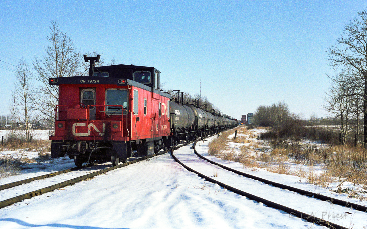 I mentioned in a previous post that the regular crew had the Coronado Sub. mostly to themselves. On Thursday's, as in this photo, a spare crew was called for the fuel run to the Cold Lake airforce base. The base required 2 trains a week to keep the planes topped up. Typically, a meet was set up close to Edmonton, Redwater often being chosen, between the returning regular crew and the spare crew heading out. In this photo, 836 is a solid train of 16 tanks, headed up by a single unit, the 5578. The grain extra can be seen in the siding at Redwater with the headlight dimmed and waiting. These meets usually happened around 11:00 with the spare crew returning late Thursday night or early Friday morning. The little siding into the culvert plant in the foreground did not have much time left. Frog and switch will be removed in the near future. Of interest, film used is Konica 100asa print film, it does look a little different than Kodak. Why the interest? If you bought 3 rolls from London Drugs, you got a little free Konica clock for your desk. It's been flipping numbers on my desk all this time (with an occasional battery change). :-)