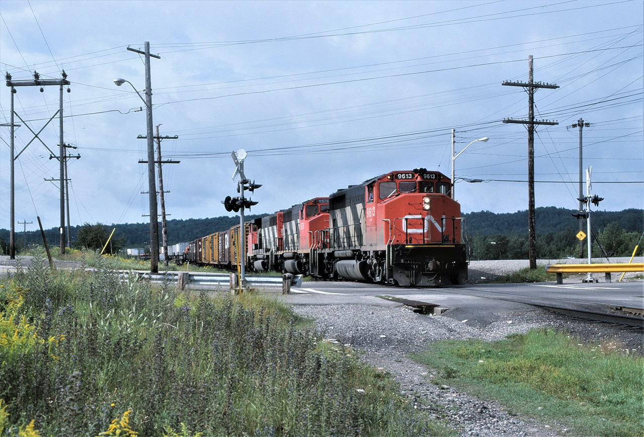 CN train 215 with very typical power, for the time period, crosses Young Street as it arrives in Capreol, Ontario on August 9, 1986.  Units are 9613-9576-9597.  The train had 69 loads 39 empties and 6994 tons.  With an HPT of 1.28, it will have no problem making track speed as it heads west.