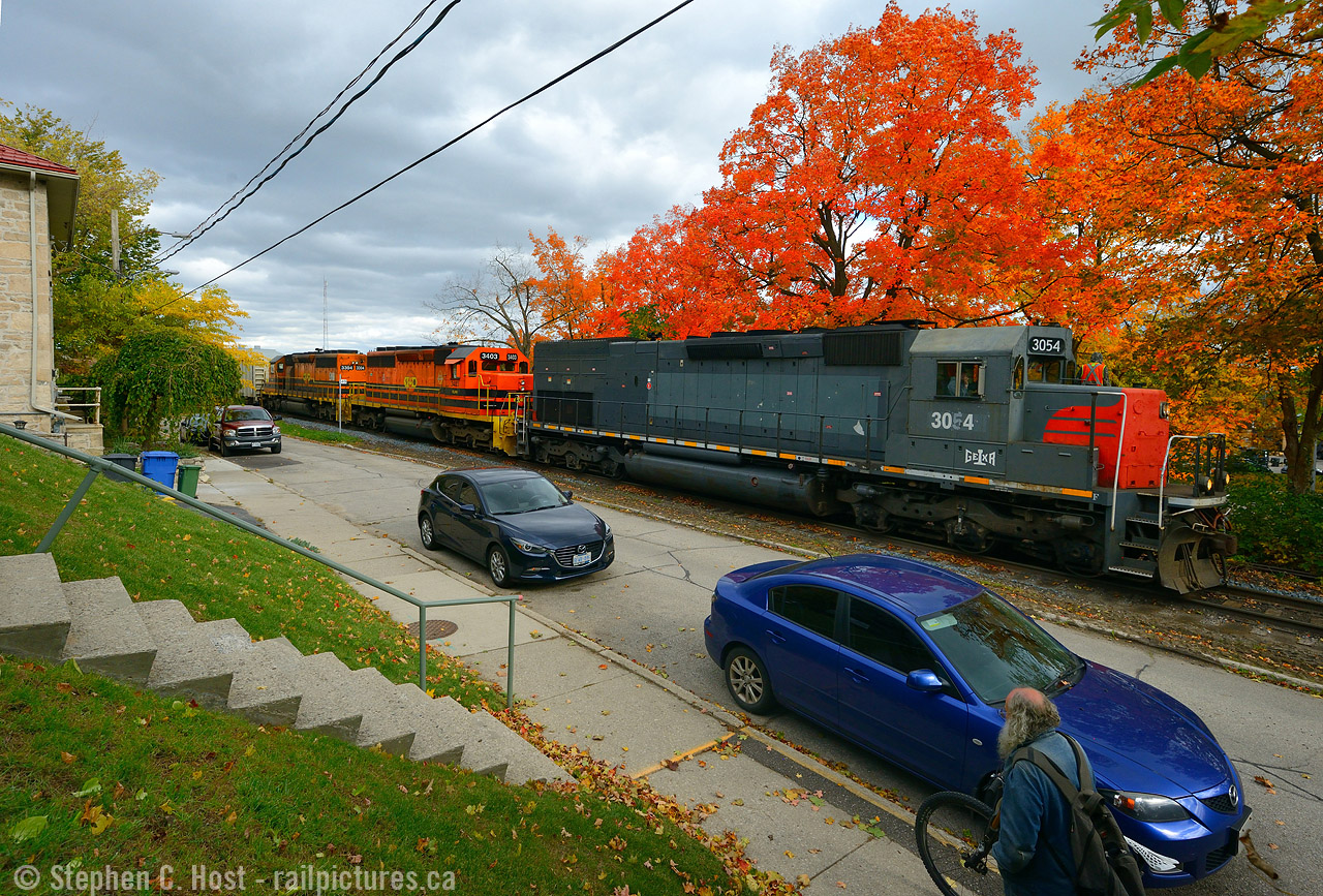 Roll on: The melodic bass of three turbocharged 6-motors rolls alongside kent on the Guelph subdivision while a pedestrian rolls his bicycle toward downtown.

Pulling one out from my crates - this is one of my favourite places in Guelph - I liked it so much I lived around here for 2 years in the early 2000's. I came across this angle while studying what I could do in the fall with GEXR on the ropes, soon to be history on the Guelph sub and I came up with this. Just as I took the photo, not only did the bike guy walk into the frame just at the right time, the hogger found me on the hillslde and gives me a slight wave from the cab. The SP nose of SD45-T2 3054 really stands out in this wide angle view.