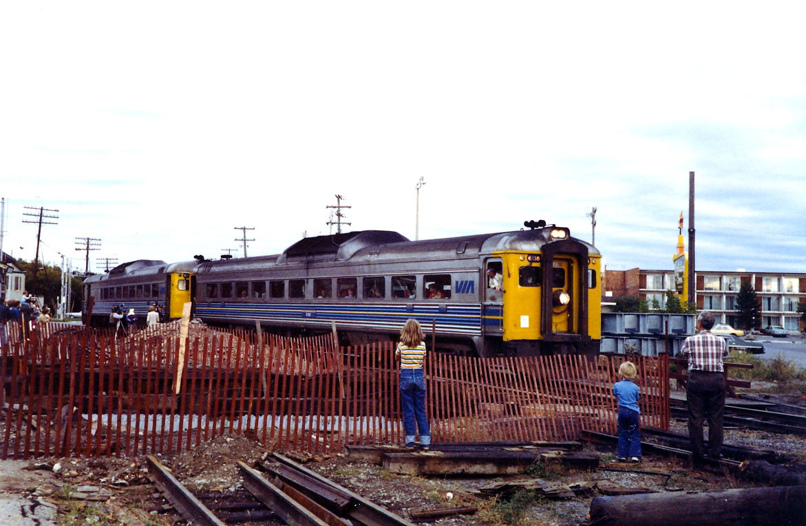 The last run of the VIA Havelock to Toronto train in 1982. At this time the replacement of the bridge over Jacksons Creek was underway with the main track severed and the old bridge removed. The lead RDC car has stopped on the diversion track adjacent to the new bridge structures on the right On the left it looks like a crew from CHEX TV is doing an interview of this event. Photo taken by my Mother.