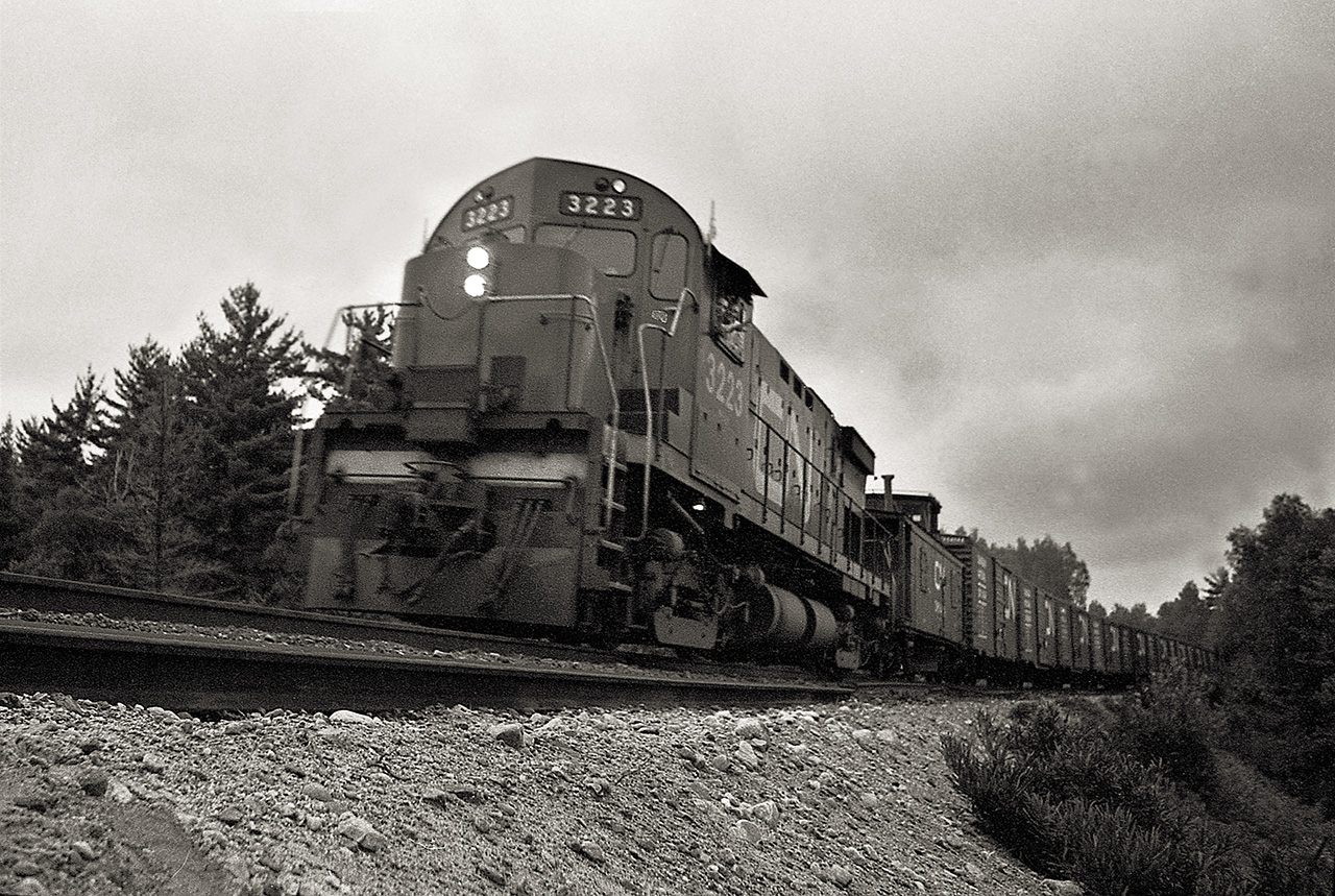 As Extra 3223 slows on its approach to Brent, an isolated crew change point on the northern edge of Algonquin park, two of the crew members poke their heads out of the side window to get their photo taken.  The first car in the consist looks to be a flanger.  The Beachburg Sub was part of the Transcontinental Mainline, built by The Canadian Northern Railway in 1915.  It was abandoned in 1995.