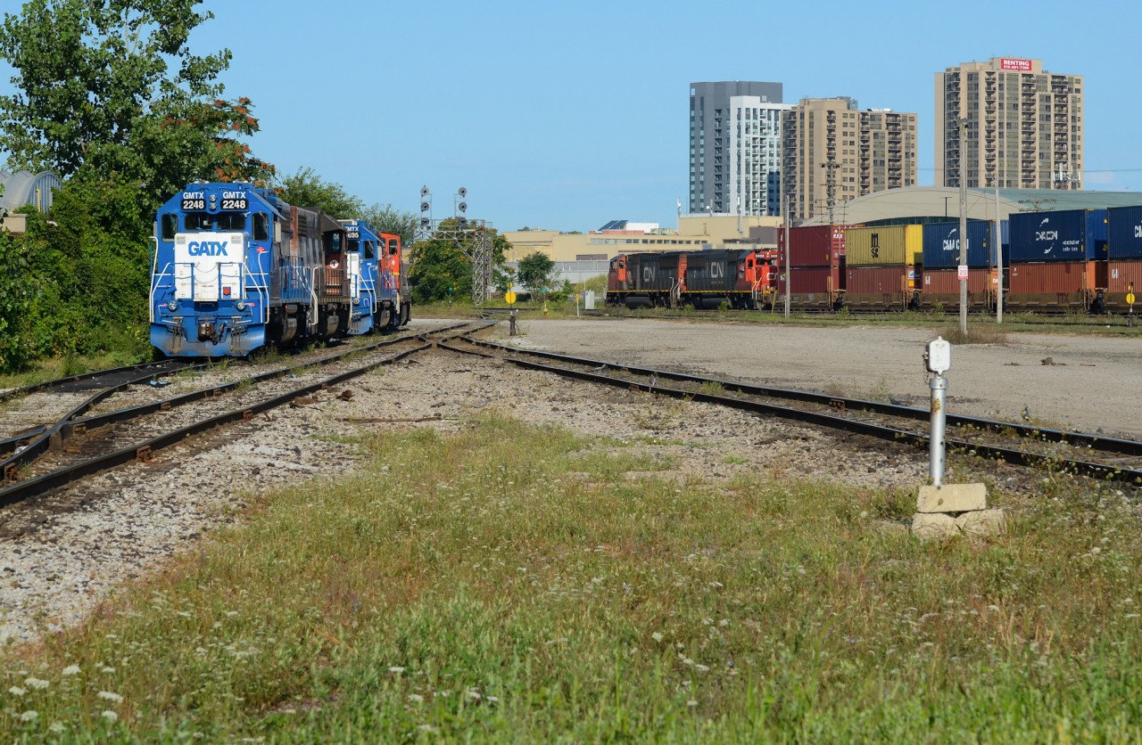 On a sunny summer morning, a CN 149 with a pair of EMD’s rolls into London with their train of double stacks for Chicago as 2 double sets of yard power sit unassigned on the west end of London Yard consisting a blue GMTX leaser on both sets. The GMTX 2695 / CN 1439 would be taken on 439 to Chatham for 514 the next day.