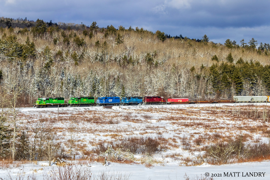 Through the winter countryside, NBSR westbound train 907 has a colorful lashup as they haul their train heading to McAdam and into Maine.