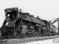 The fireman of CNR U-2-a 6105, one of the earliest Confederation type locomotives built for the Canadian National Railways by the Canadian Locomotive Company in July of 1927, is busy atop the tender at Hamilton yard taking on water from the standpipe.  6105 was the first Confederation on CNR to be built with a booster engine, the prior 6100 – 6104 were built without, though 6100 briefly had one installed for display at Baltimore’s <i>Fair of the Iron Horse</i> in October 1927.  These boosters, mounted on the rear axle of the trailing truck beneath the cab, were used to start a heavy train or operate at low speed under certain conditions using the excess steam that is created though not used at low speeds.  6105 would be scrapped in February 1960.  Note the building at upper right on Bay Street, today the home of Hutch’s Harbour Front fish & chip restaurant (2nd location), built circa 1940.