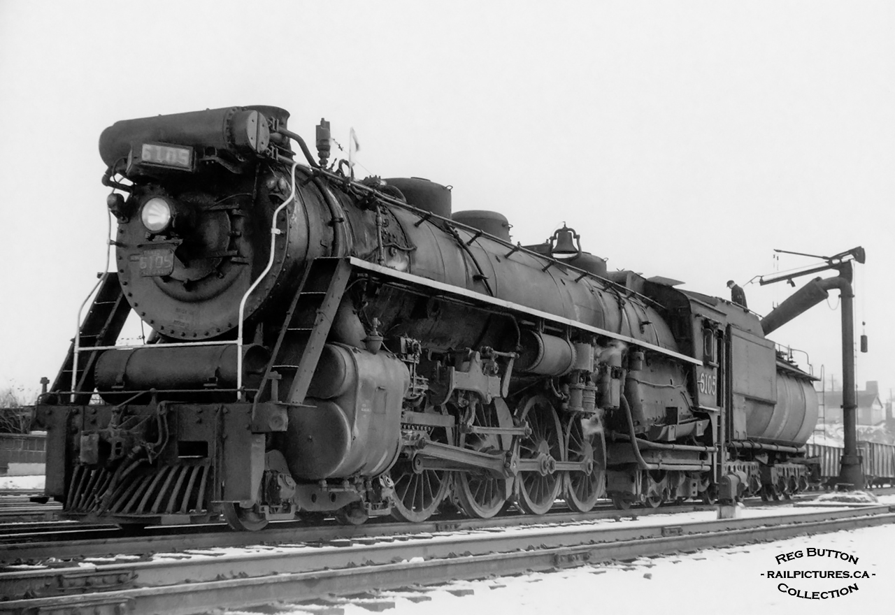 The fireman of CNR U-2-a 6105, one of the earliest Confederation type locomotives built for the Canadian National Railways by the Canadian Locomotive Company in July of 1927, is busy atop the tender at Hamilton yard taking on water from the standpipe.  6105 was the first Confederation on CNR to be built with a booster engine, the prior 6100 – 6104 were built without, though 6100 briefly had one installed for display at Baltimore’s Fair of the Iron Horse in October 1927.  These boosters, mounted on the rear axle of the trailing truck beneath the cab, were used to start a heavy train or operate at low speed under certain conditions using the excess steam that is created though not used at low speeds.  6105 would be scrapped in February 1960.  Note the building at upper right on Bay Street, today the home of Hutch’s Harbour Front fish & chip restaurant (2nd location), built circa 1940.