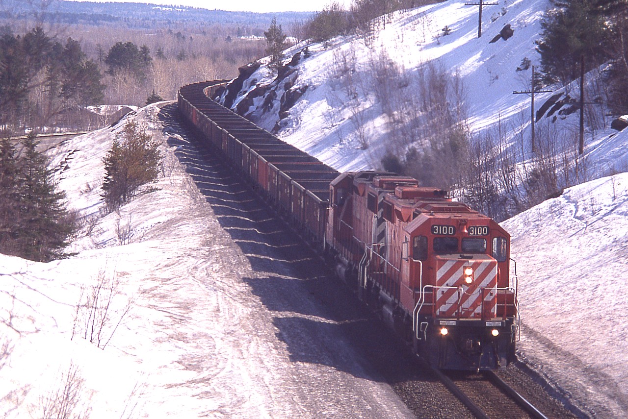 CP's reliable workhorse GP38-2 locos #3100 and 3089 are seen on the hillside along Highway 144 a few miles south of namesign CP Levack with a load of empties for the mine at Onaping Falls/Levack on a warm spring afternoon. This is around the perfect time of the year for photos up in the Greater Sudbury region in my opinion. Usually some snow to cover the dull grounds of early spring, but often warm enough to shed the winter coat. And NO bugs.
(The location of this photo is approximately opposite of a scenic spot called "high Falls")