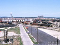 Here's a sunny afternoon view of CP's Toronto Yard (a.k.a. Agincourt Yard) on July 2nd 1978, as viewed looking east from the General Yard Office. Visible are the Car Shops and repair yards, Diesel Shop and servicing areas (and its water tower), and the West Receiving and East Recieving yards to the right. Markham Road is visible in the distance, and the two mainline tracks of the Belleville Sub pass under it on the far right side of the underpass. On the left is the Retarder tower, and part of the sprawling Classification Yard tracks. 
<br><br>
Scarborough's suburban housing sprawl is present in the distance, swallowing up land that was once rural farmland and fields that existed all around the yard when it was originally built <a href=http://jpeg2000.eloquent-systems.com/toronto.html?image=ser12/s0012_fl1961_it0217.jp2><b>"out in the boonies"</b></a> in the early 60's.
<br><br>
The Car Shop yard is dominated by "home road" CP cars, the most visible are tonnes classic 40' boxcars in stepped lettering (1950's), script lettering (1960's) and action red (1970's). Baggage cars in OCS service and  vans (cabooses) are also present.
<br><br>
<i>Bill McArthur photo, Dan Dell'Unto collection slide</i>.