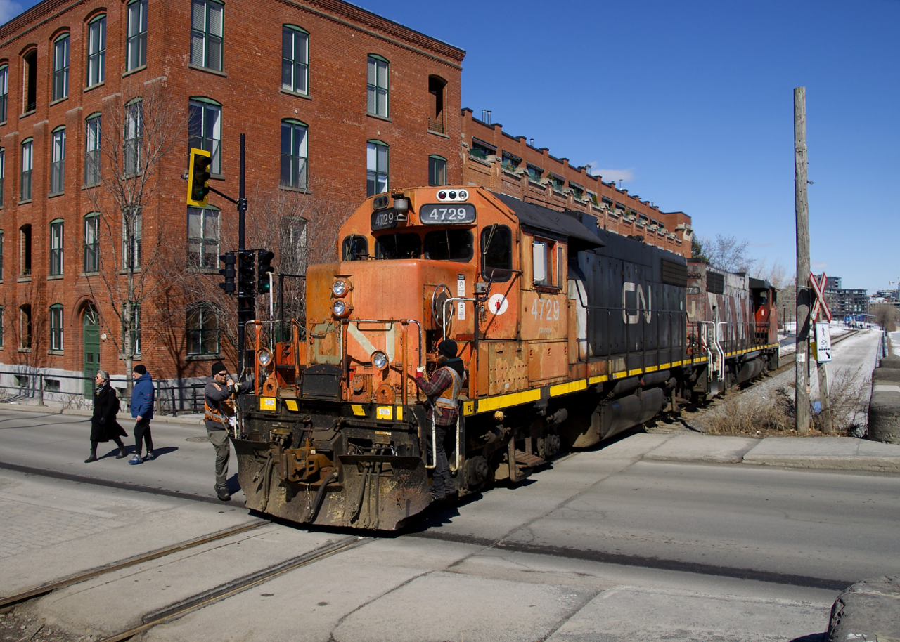 Two crewmembers have just gotten back on CN 4729 after flagging Charlevoix Street. Their train had just dropped off six grain cars at Ardent Mills. The building behind was once a Stelco factory and is now condos.