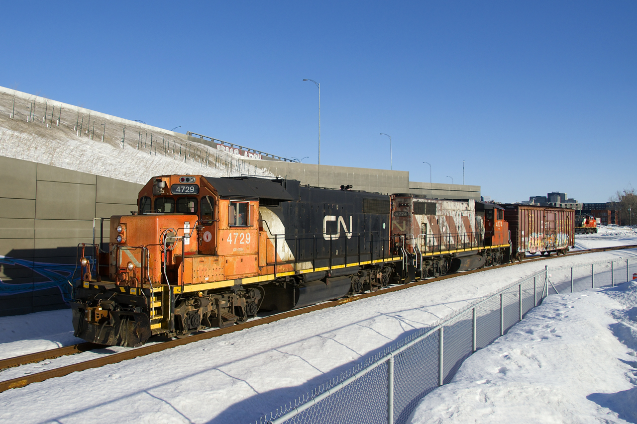 The Pointe St-Charles switcher has a single boxcar for Kruger on the Turcot Holding Spur as it approaches the level crossing at Notre-Dame Street. At left is part of the recently finished and reconstructed Turcot interchange. Barely visible at right is the leader of grain train CN 878, temporarily stopped on the Montreal Sub.