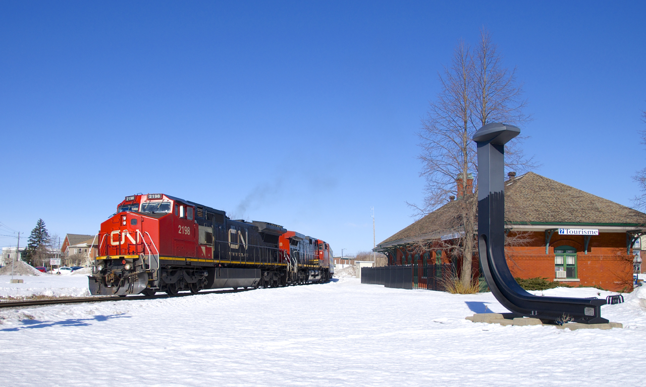 CN 324 with CN 2198 & CN 2528 is passing the ex-Grand Trunk station in St-Jean-sur-Richelieu. At right is an oversized spike to commemorate how this was the terminus of Canada's first railway (the Champlain and St. Lawrence Railroad).